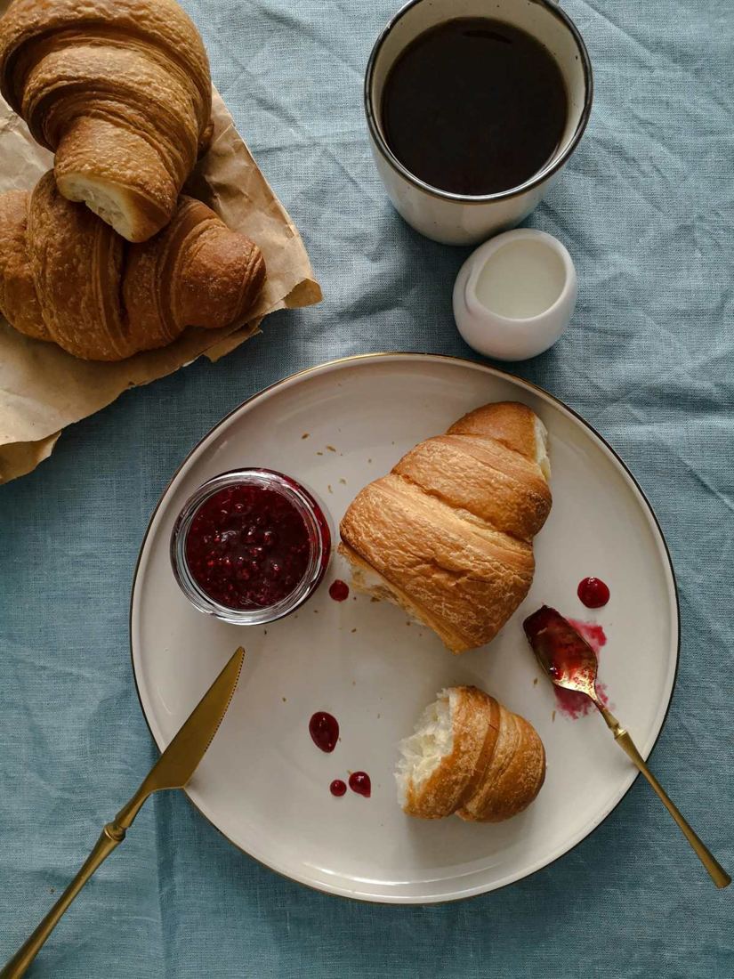 Colazione dall'alto: croissant, caffè, burro e marmellata su una tovaglia azzurra